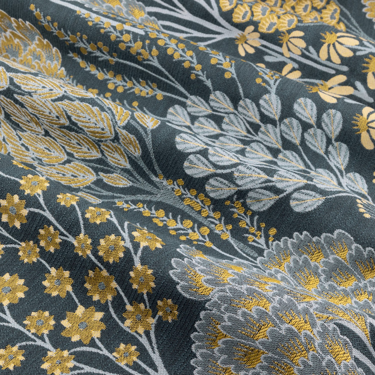 Close-up of Ophelia jacquard eyelet curtain fabric, showing woven saffron yellow and pale grey floral trees and daisies on a deep blue-teal ground.