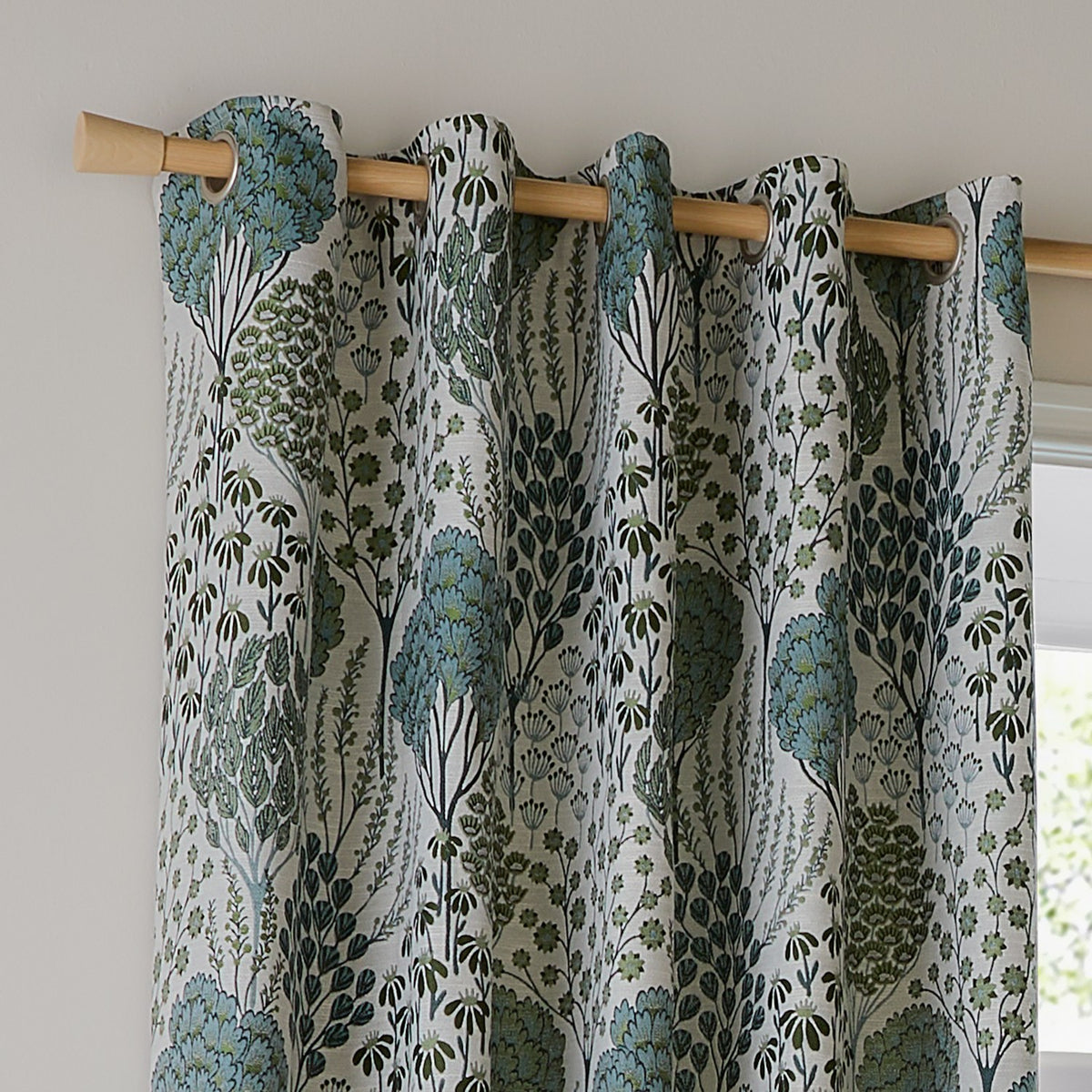 Ophelia Jacquard eyelet curtains in Thyme/Mineral, fully lined with a woven floral pattern in blue-green and forest tones on cream, hung on a wooden pole by a window.