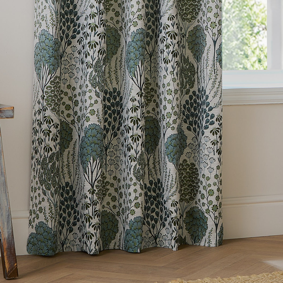 Ophelia Jacquard fully lined eyelet curtains in Thyme/Mineral, showing a woven floral pattern in blue-green and forest tones on cream, hanging beside a window.