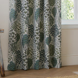 Ophelia Jacquard fully lined eyelet curtains in Thyme/Mineral, showing a woven floral pattern in blue-green and forest tones on cream, hanging beside a window.
