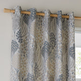 Ophelia Jacquard fully lined eyelet curtains in Wedgewood, showing a woven floral tree and daisy pattern in slate blue, gold and taupe on a pale ground, hung on a wooden pole.
