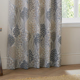 Ophelia Jacquard Fully Lined Eyelet Curtains in Wedgewood, showing a floral tree jacquard weave in slate blue, soft gold and taupe, draped in a living room by a window.