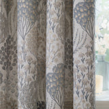 Ophelia Jacquard Fully Lined Eyelet Curtains in Wedgewood, close-up of pale fabric with woven floral jacquard trees and daisies in slate blue, gold and taupe, shown beside a window with a glass vase.