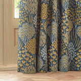 Ophelia Jacquard Pencil Pleat Curtains in blue and saffron, woven floral and tree motif, pooling in folds beside a wooden door in a home setting.