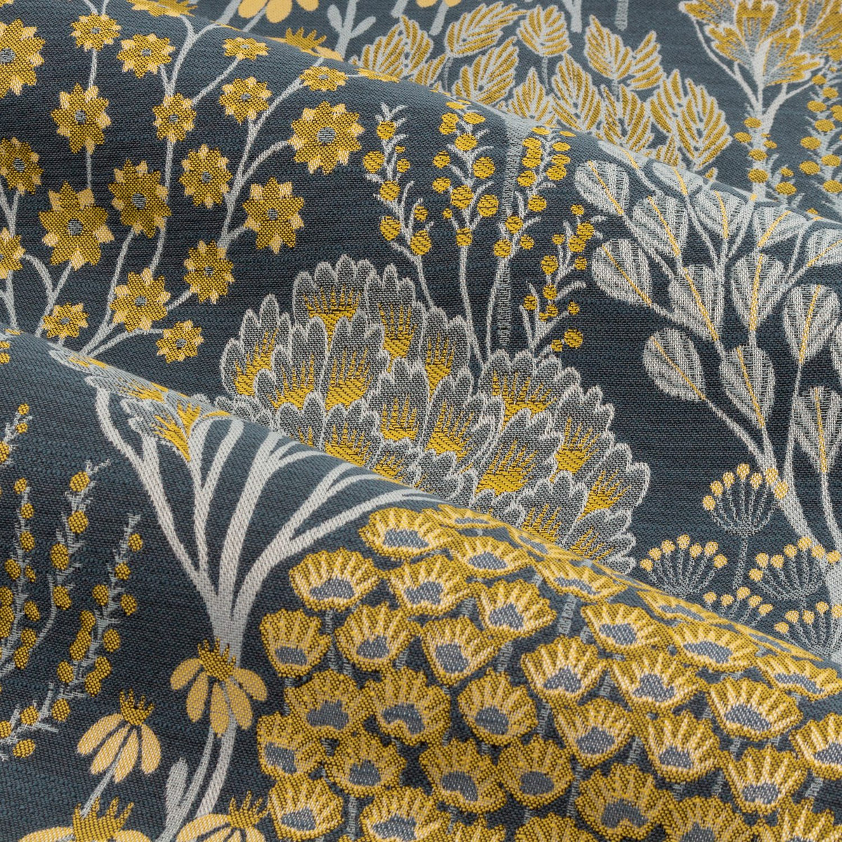 Close-up of Ophelia Jacquard Pencil Pleat Curtains fabric, showing a woven floral and botanical pattern in saffron gold and grey tones on a deep teal-blue polyester ground.