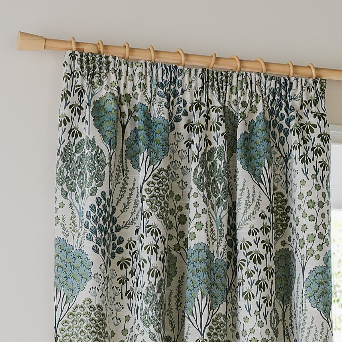 Ophelia jacquard pencil pleat curtain in Thyme/Mineral, showing botanical tree and floral pattern in green and blue-grey on cream, hung on a wooden pole with rings.