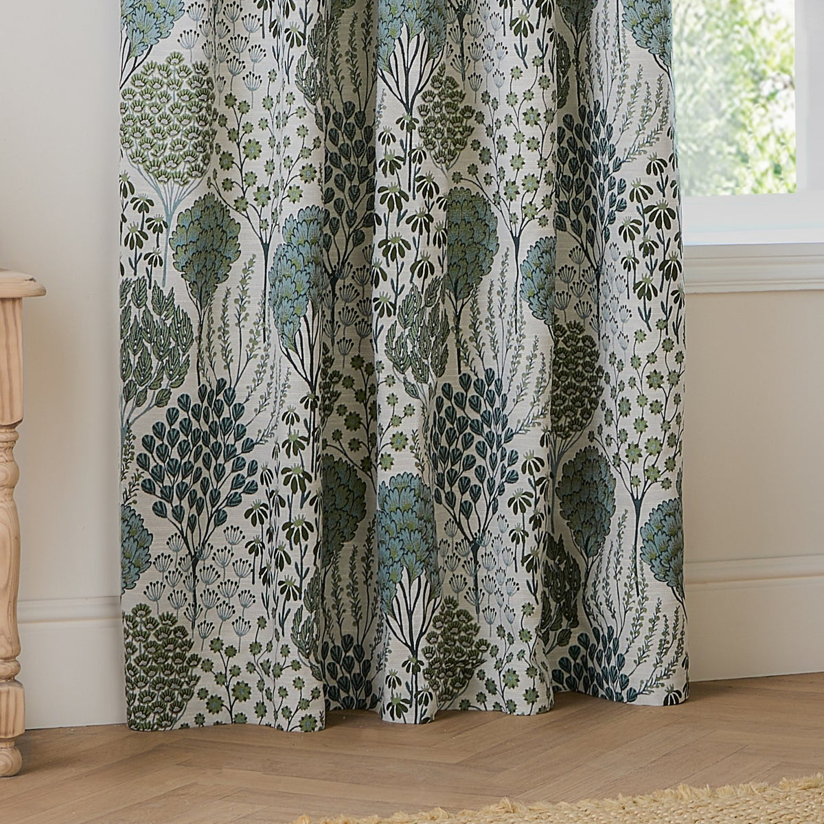 Ophelia Jacquard pencil pleat curtains in Thyme/Mineral, showing woven botanical tree and floral pattern in green and blue-grey on cream, draped in a living room by a window.