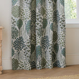 Ophelia Jacquard pencil pleat curtains in Thyme/Mineral, showing woven botanical tree and floral pattern in green and blue-grey on cream, draped in a living room by a window.