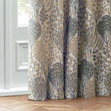 Ophelia Jacquard Polyester Pencil Pleat Curtains in Wedgewood, pencil pleat fabric folds showing a botanical jacquard pattern of trees and flowers in blue and beige, near a glass door.