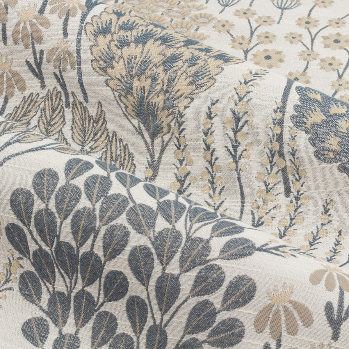 Close-up of Ophelia Jacquard pencil pleat curtain fabric in Wedgewood, showing a woven botanical pattern of stylised trees, seed heads and flowers in blue and beige on a pale polyester ground.