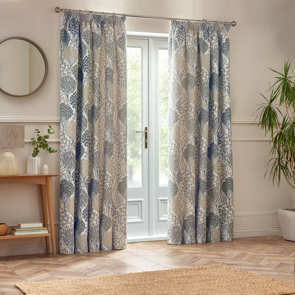 Ophelia Jacquard Polyester Pencil Pleat Curtains in Wedgewood blue, botanical jacquard design in blue and beige, hung pencil pleat style beside a glazed door in a living room.