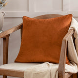 Opulence Plain Velvet Cushion in ginger orange with piped edges, square shape, styled on a wooden armchair with a cream knit throw.