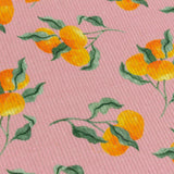 Close-up of a pink polyester placemat with a digitally printed orange fruit and green leaf pattern, showing its woven ribbed texture.