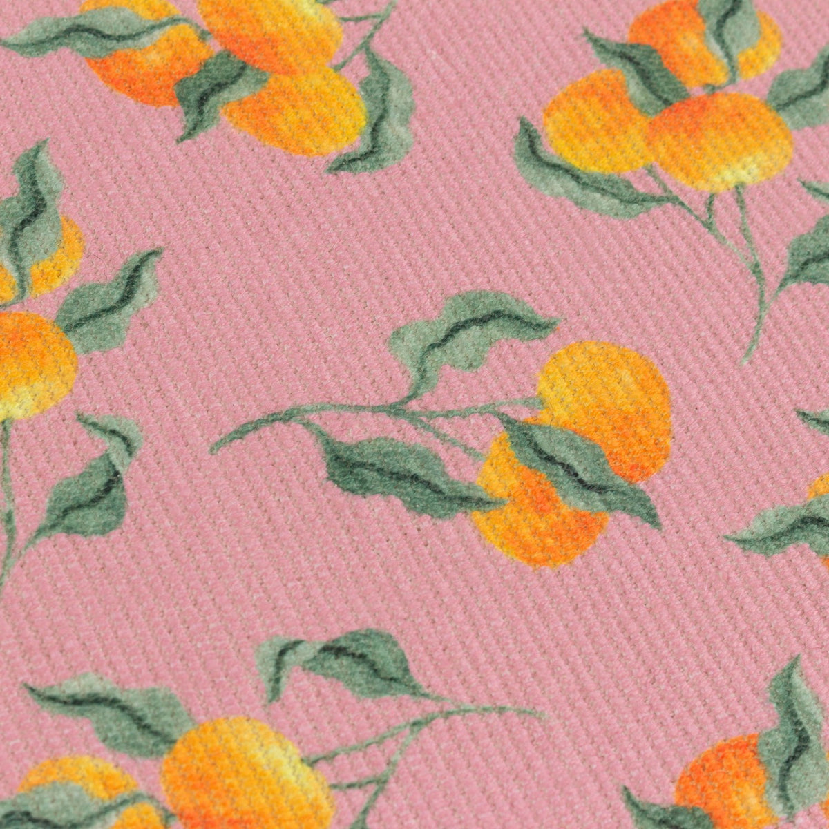 Close-up of a pink polyester table runner with a scattered orange fruit and green leaf print on a woven textured fabric.