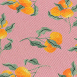Close-up of a pink polyester table runner with a scattered orange fruit and green leaf print on a woven textured fabric.
