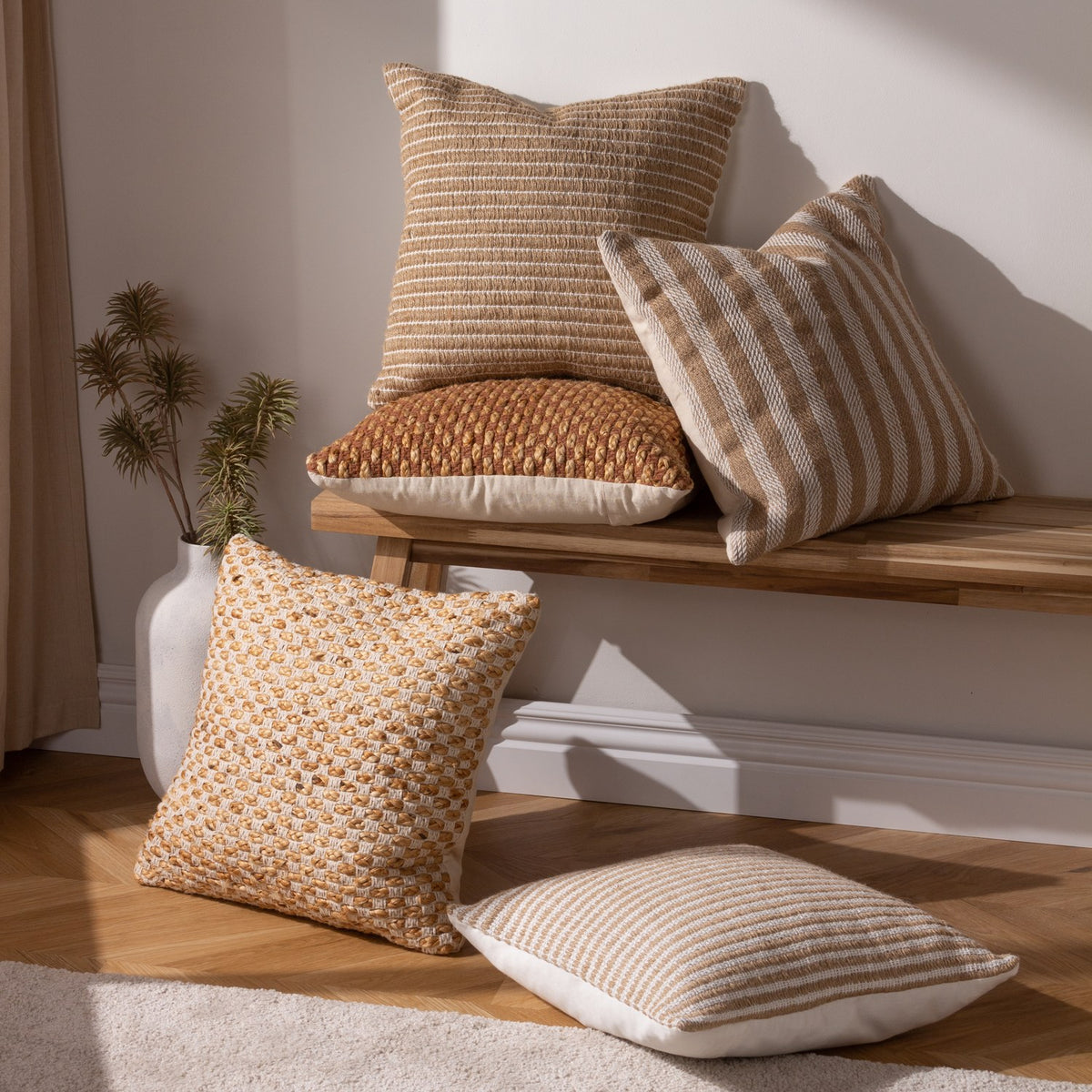 Organik Plain Cotton Cushion in Natural, striped textured square cushion woven from jute and cotton, shown on a wooden bench with patterned cushions in a sunlit living room.