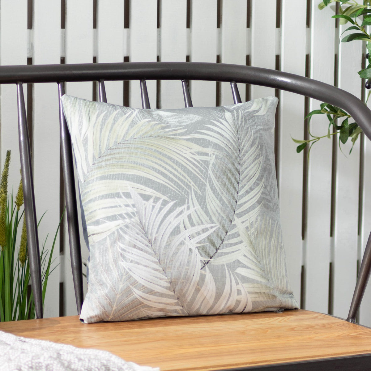 Palma Reversible Polyester Cushion in green, square with tonal botanical leaf print, shown on a metal-framed bench against white slatted panelling.