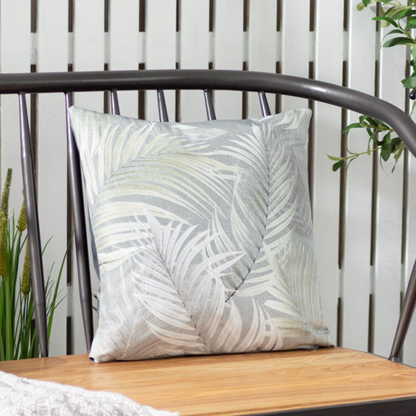 Palma Reversible Polyester Cushion in green, square with tonal botanical leaf print, shown on a metal-framed bench against white slatted panelling.