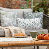 Rectangular Palma cushions with green tonal leaf and fern prints on grey outdoor sofa, styled with a cream throw on a garden patio.