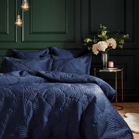Palmeria Velvet Jungle Duvet Cover Set in navy on a bed, showing quilted velvet fabric with a raised leaf design, styled in a bedroom with a dark green panelled wall.