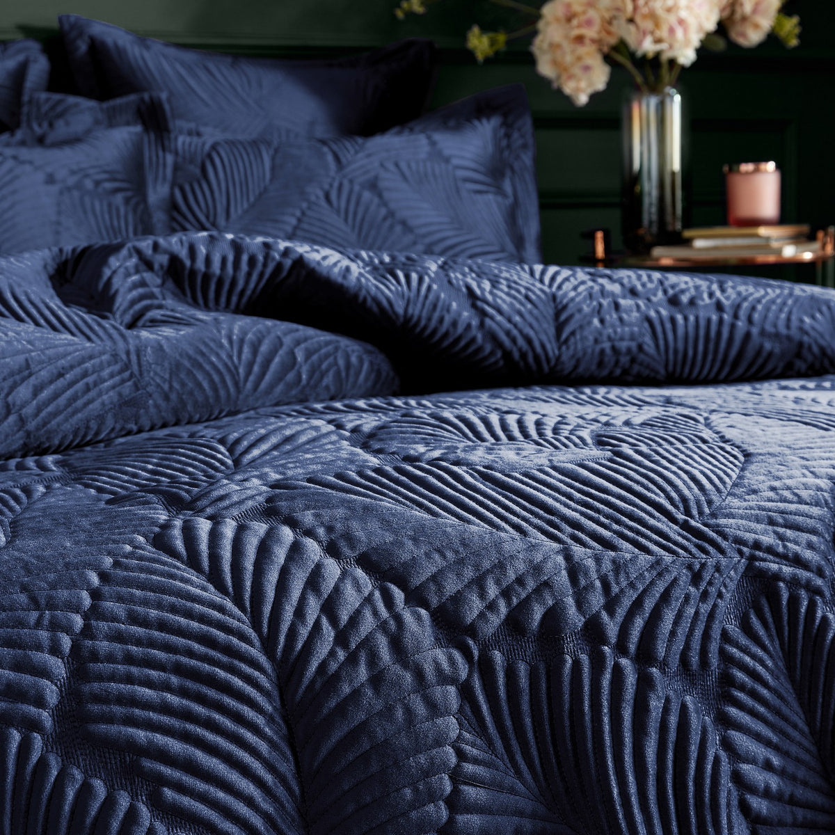 Palmeria Velvet Jungle Duvet Cover Set in navy, showing quilted velvet fronds on pillowshams and duvet, styled on a bed with flowers in the background.