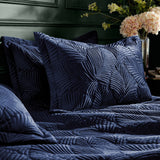 Palmeria Velvet Jungle Duvet Cover Set in navy on a bed, with matching quilted pillow shams showing raised leaf-pattern stitching, set in a bedroom with dark green panelled wall.