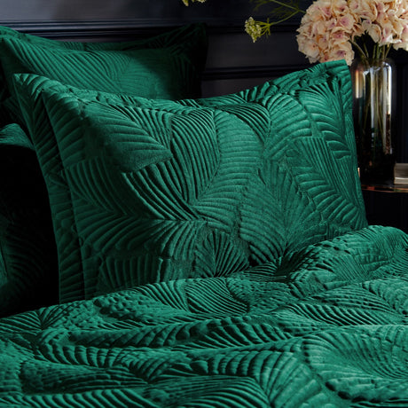 Palmeria Velvet Cotton Pillowcase Pair in emerald green, quilted palm-leaf pattern on velvet, styled on a bed with matching quilted bedding in a dark bedroom setting.