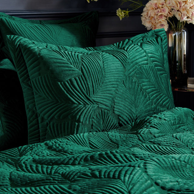 Palmeria Velvet Cotton Pillowcase Pair in emerald green, quilted palm-leaf pattern on velvet, styled on a bed with matching quilted bedding in a dark bedroom setting.