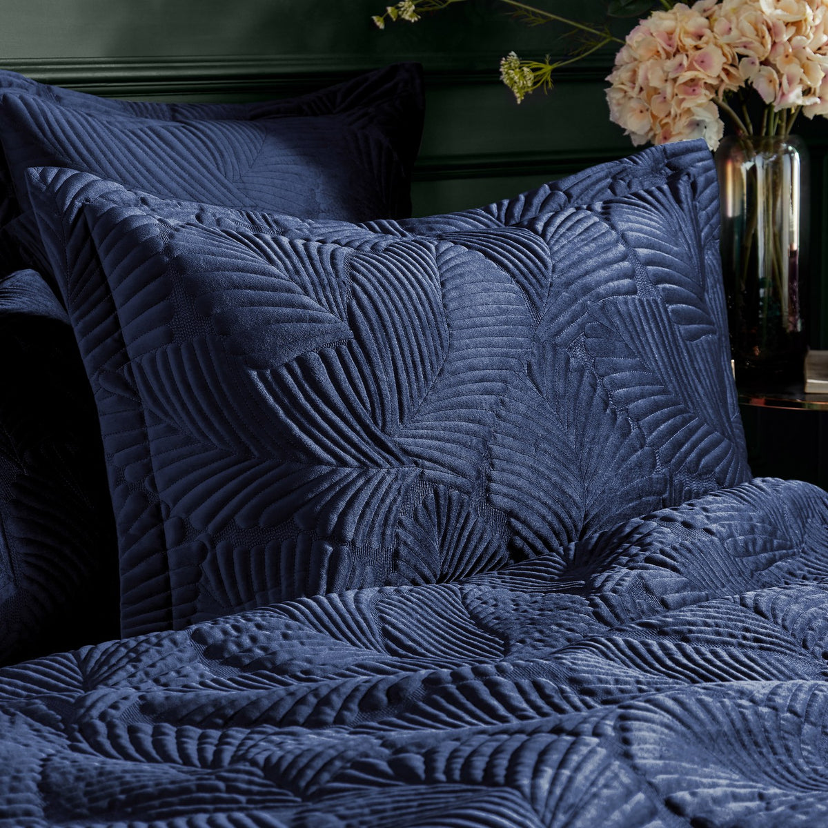 Palmeria Velvet Cotton Pillowcase Pair in navy, shown on bedroom pillows with a quilted, embroidered palm-leaf texture on the velvet front.