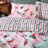 Passport To The North Pole duvet cover set in Candy Floss/Linen with pink Santa-print pillowcases and duvet reversing to a red mistletoe stripe, styled on a bed with a green headboard.