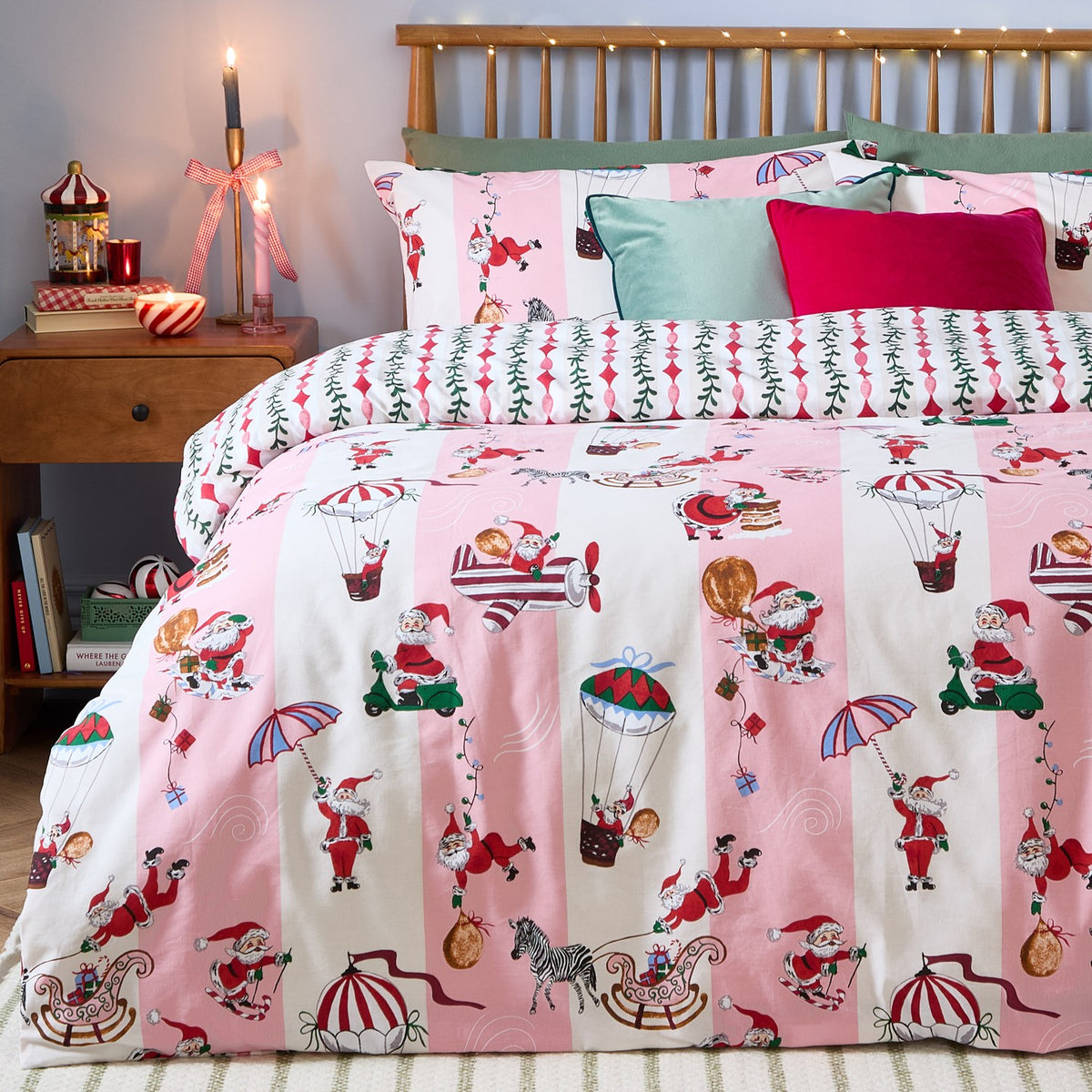 Passport To The North Pole Striped Duvet Cover Set in Candy Floss/Linen on a bed, featuring pink and cream stripes with Santa scenes, styled with green and pink cushions in a festive bedroom.
