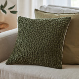 Pebble Linen Chenille Cushion in Lichen olive green with a textured pebble-like chenille surface, shown on a light sofa beside neutral scatter cushions.