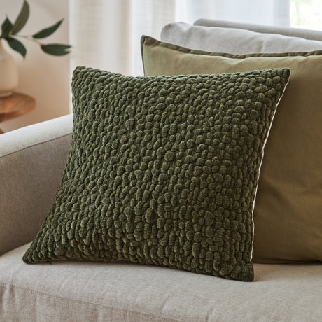 Pebble Linen Chenille Cushion in Lichen olive green with a textured pebble-like chenille surface, shown on a light sofa beside neutral scatter cushions.