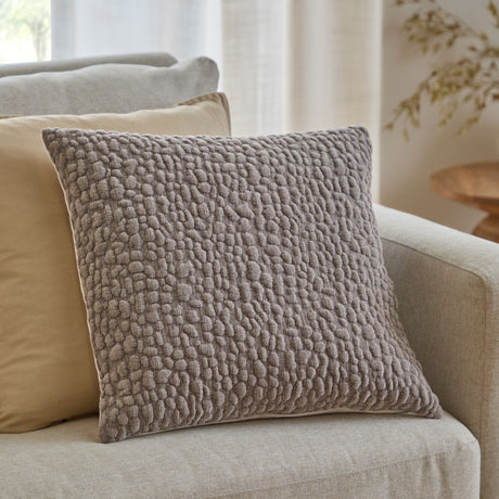 Pebble Linen Chenille Cushion in slate grey with a raised pebble-textured front, styled on a beige sofa alongside a mustard cushion in a living room setting.