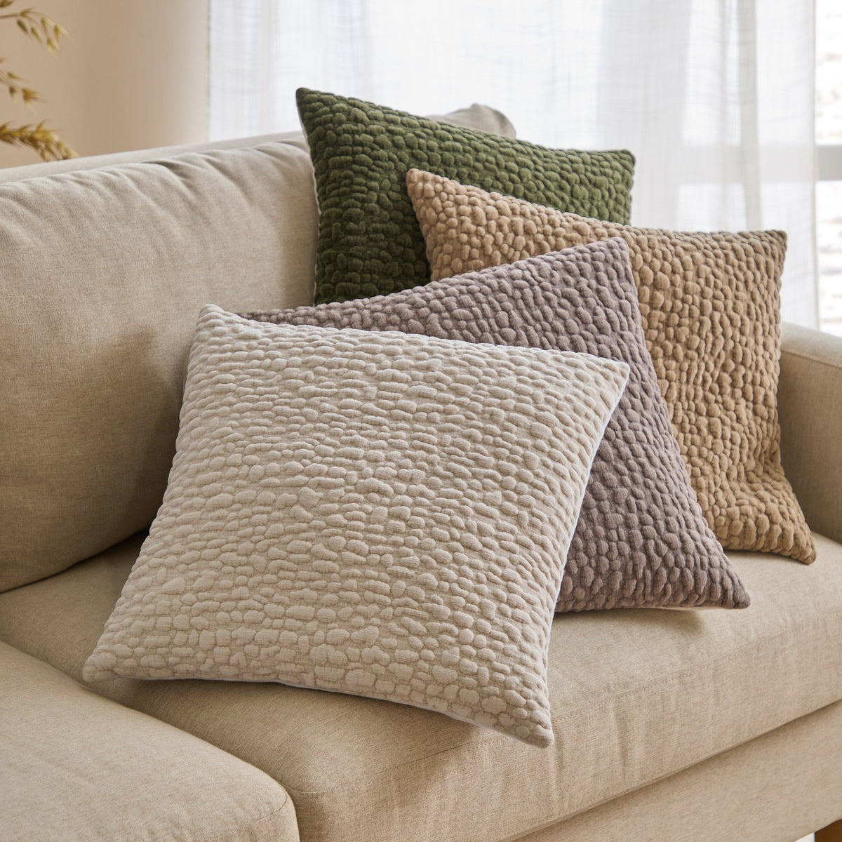 Pebble Linen Chenille Cushion in Slate, a square scatter cushion with a textured pebble-like chenille front, shown with cream, taupe and green cushions on a beige sofa.