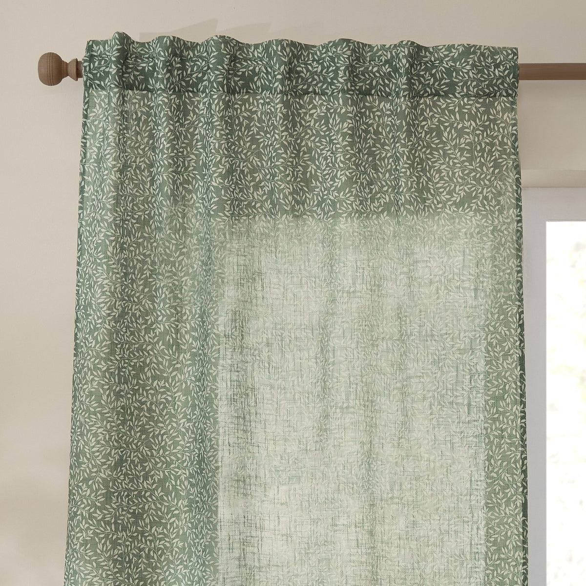 Perrie Leaf Floral Polyester Curtain Panel in forest green with a sheer, open-weave texture and back tab heading, hung from a wooden rod near a window.