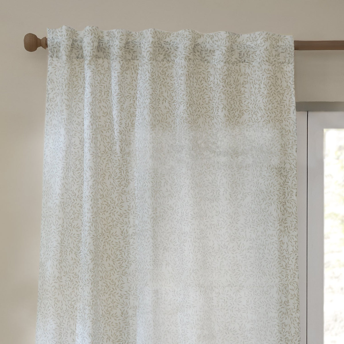 Perrie Leaf Floral Polyester Curtain Panel in natural hangs from a wooden pole with tab-top heading, showing a small trailing leaf print on a pale sheer fabric beside a window.