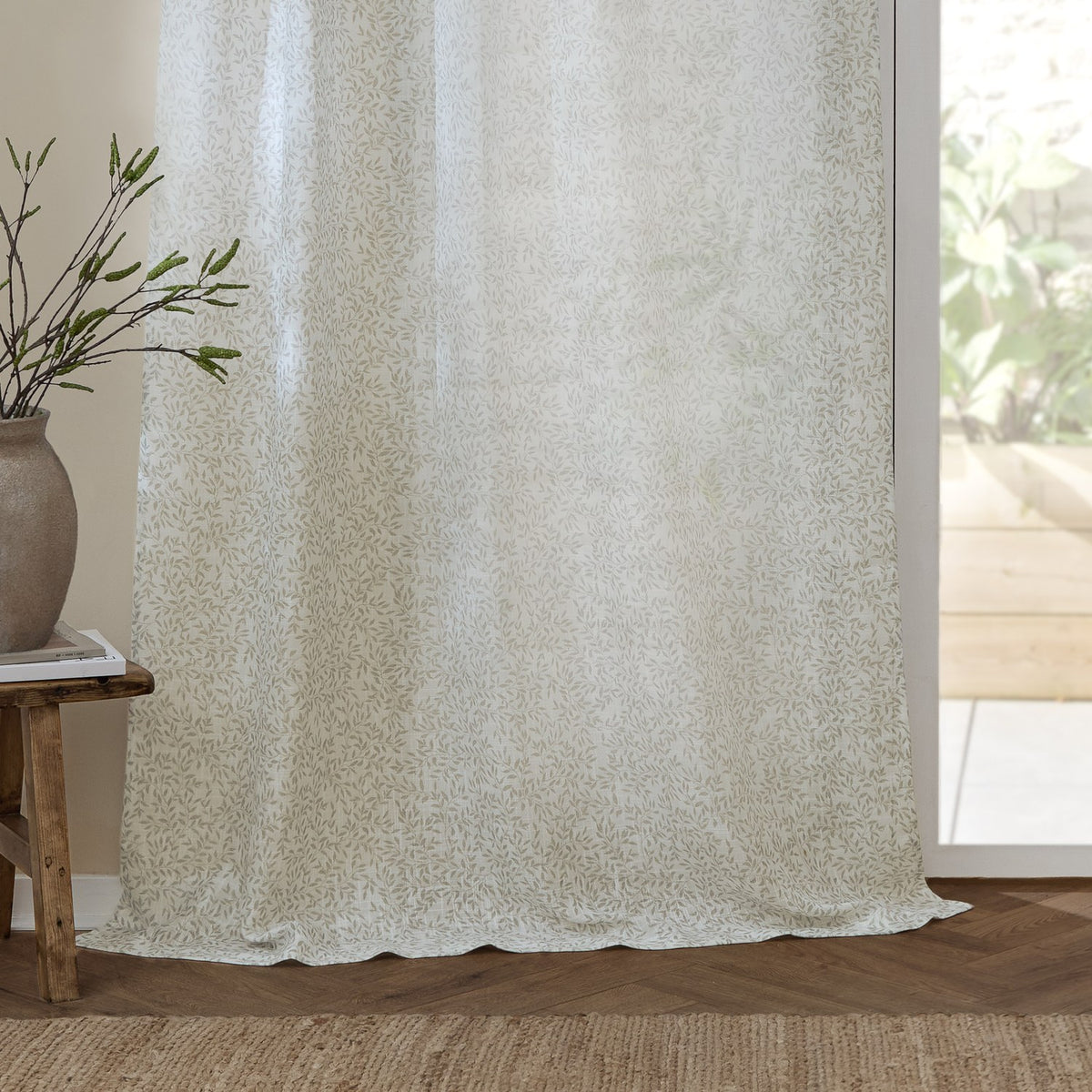 Perrie Leaf Floral Polyester Curtain Panel in natural, semi-sheer fabric with a small trailing leaf print, hung by a bright glass door in a living room setting.