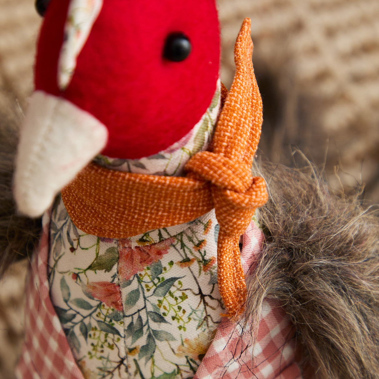 Close-up of the Phineas Polyester Door Stop, a sitting bird design with red felt head, black bead eyes, pale beak, floral jacket, rust-orange knotted scarf, and grey feathery tail.