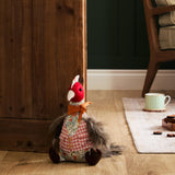 Phineas Polyester Door Stop shaped like a sitting bird with red felt head, floral jacket, pink gingham waistcoat, rust scarf and grey feathery tail, shown beside a wooden door in a living room.