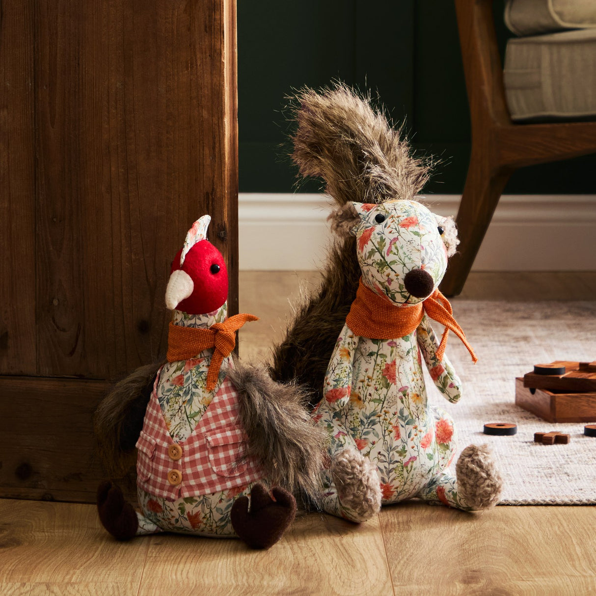 Phineas Polyester Door Stop shown as a sitting bird in floral fabric with red felt head, pink gingham waistcoat, rust-orange scarf, and feathery grey tail, beside a matching squirrel design on a rug.