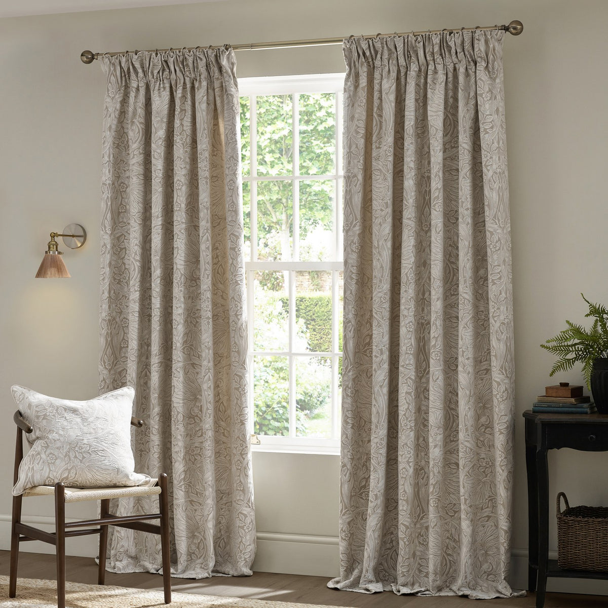 Pimpernel Jacquard Linen pencil pleat curtains in beige floral pattern, shown pencil-pleat headed on a pole beside a window in a living room setting.