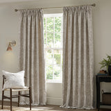 Pimpernel Jacquard Linen pencil pleat curtains in beige floral pattern, shown pencil-pleat headed on a pole beside a window in a living room setting.