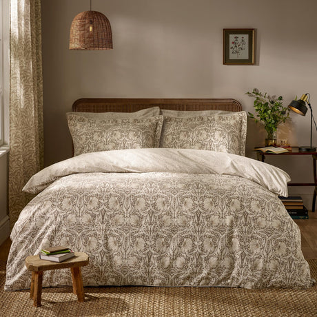 Pimpernel Cotton Floral Duvet Cover Set in natural and chocolate, shown on a bed with matching pillowcases in a bedroom with rattan headboard, wicker pendant light, and framed botanical print.
