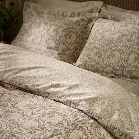 Pimpernel Cotton Floral Duvet Cover Set in natural and chocolate, shown on a bed with matching pillowcases featuring a Morris floral pattern in a bedroom setting.