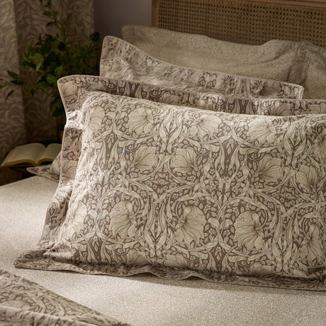Pimpernel Percale Cotton Pillowcase Pair in natural and chocolate, showing a winding floral pattern in soft browns on cotton bedding, styled on a bed with matching sheets.