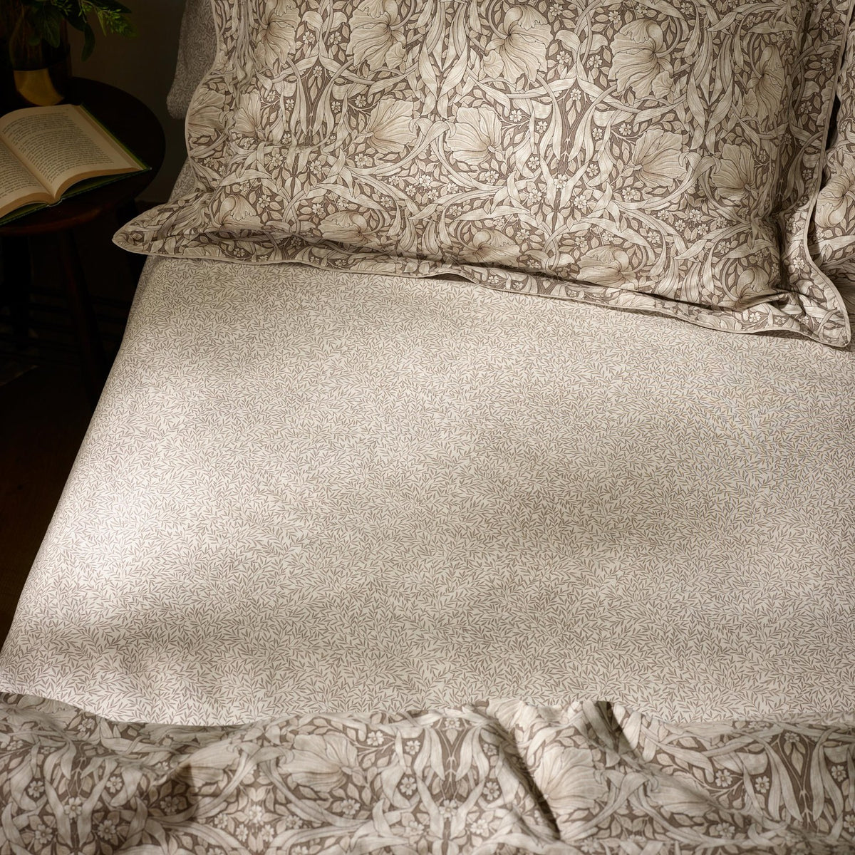 Pimpernel Percale Cotton Fitted Sheet in natural and chocolate, small-scale leaf print on cream cotton, shown on a bed with matching pillowcases and floral duvet.