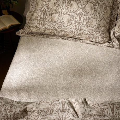 Pimpernel Percale Cotton Fitted Sheet in natural and chocolate, small-scale leaf print on cream cotton, shown on a bed with matching pillowcases and floral duvet.