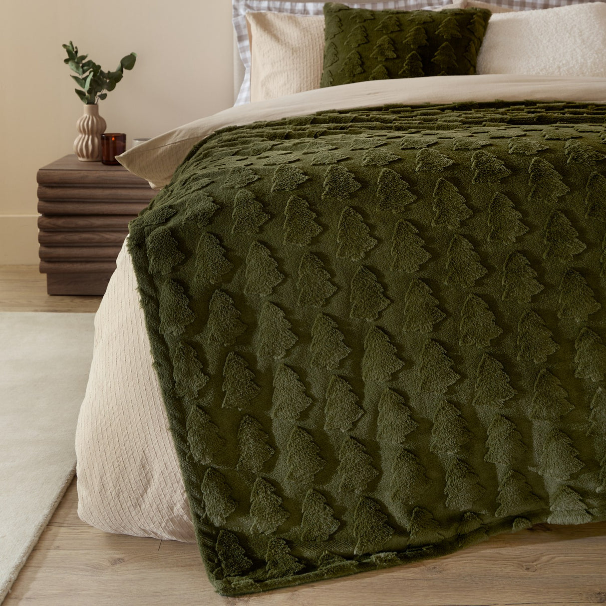 Pines Velvet Faux Fur Throw in forest green draped over a bed, showing raised tree-textured pile alongside cream bedding and a matching cushion.