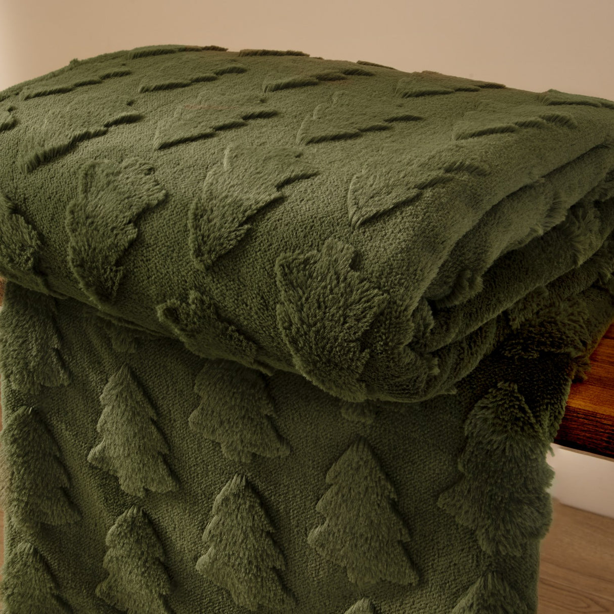 Pines Velvet Faux Fur Throw in forest green, folded over a wooden surface showing a raised tufted tree pattern on faux fur with a smooth velvet reverse.